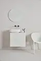 Weißer Wand-Waschtisch mit runder Keramikschüssel, darunter eine schlichte weiße Ablage. Helle Wand mit einem runden Spiegel und zwei schwarzen Wasserhähnen von Ideal Standard.
